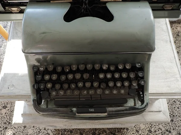 An old gray typewriter with white Cyrillic letters on black keys and one missing key. Closeup photo