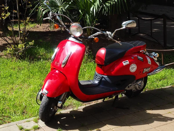 Russland, Sotschi 01.05.2021. Rotes, neues, glänzendes Moped parkt unter gleißender Sonne auf Pflasterplatten in der Nähe des Rasens — Stockfoto