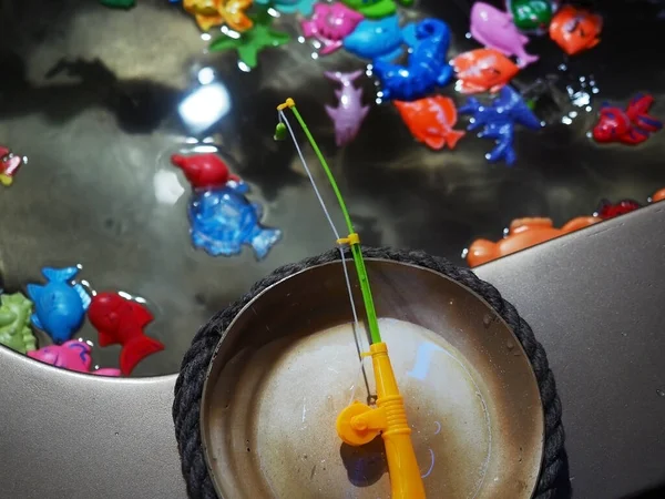 Een speelgoedhengel hangt boven een miniatuurbad met plastic kleurrijke vissen. Kinderspel — Stockfoto