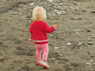 Küçük sarışın çocuk bulutlu serin bir günde kumlu sahilde yürüyor.