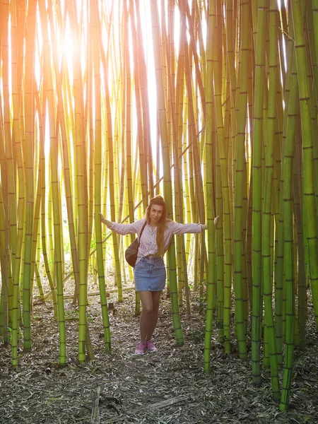 Smiling girl standing in bamboo grove holding tree trunks on warm spring day — 스톡 사진