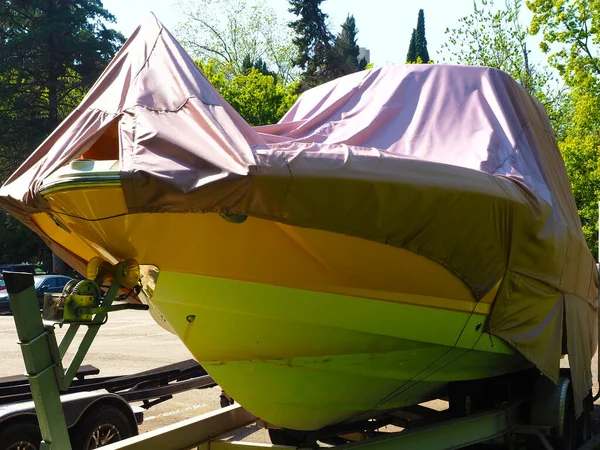 A yellow boat covered with a cape stands on a street road on a sunny summer day