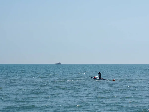 Homem em sapsurf no mar sob céus claros em uma tarde ensolarada — Fotografia de Stock