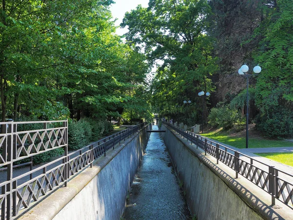 A narrow river fenced with borders on both sides in a green shady park — Foto de Stock