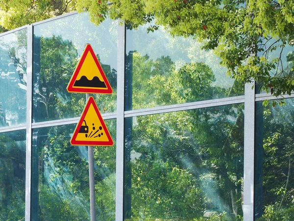 Жовтий подвійний трикутний попереджувальний дорожній знак на стовпі біля прозорого паркану в літній сонячний день — стокове фото