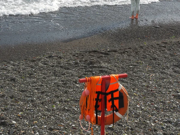 Equipamento de resgate laranja pendura na praia de seixos do mar espumoso — Fotografia de Stock