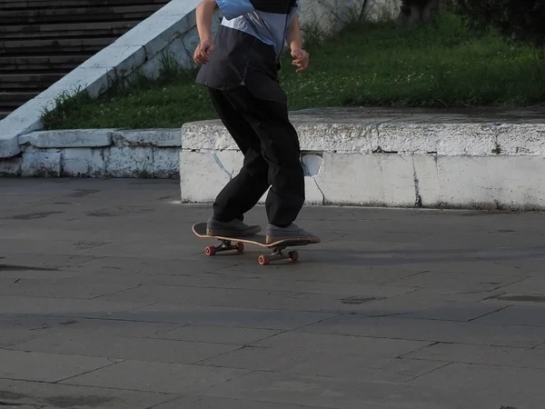 A teenager rides a skateboard on a granite tiled area along the curb — Stock Photo, Image