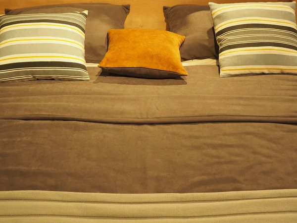 Fragment eines Bettes mit gestreiften und monochromen quadratischen Kissen und einer Decke in Graubrauntönen — Stockfoto
