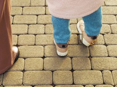 Spor ayakkabılı ve mavi pantolonlu çocuklar kaldırım levhalarında duruyorlar.