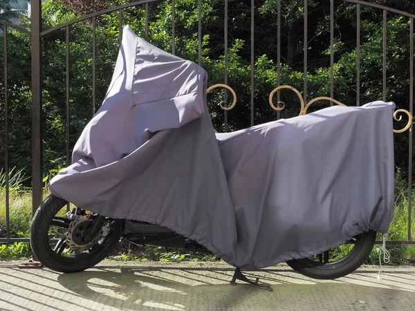 Egy napellenzővel borított motorkerékpár áll egy kovácsolt kerítés mellett a parkban — Stock Fotó