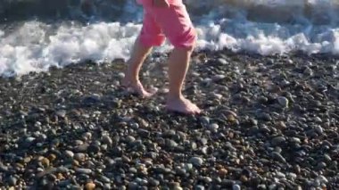 Deniz köpüklü dalgalarla yıkanmış çakıl taşı sahilinde yürüyen bir kızın bacakları.
