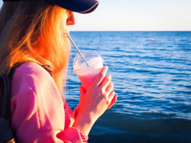 Kız denizin arka planındaki tüpten pembe bir milkshake içiyor.