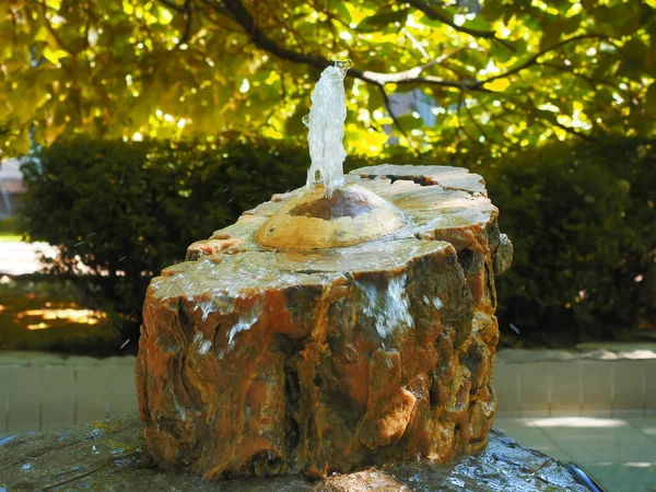 Um pequeno fluxo da fonte jorra de um toco de pedra decorativa. Fonte decorativa no parque — Fotografia de Stock