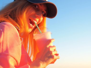 Şişkin gözlü ve ağzı açık bir kız elinde sütlü pembe bir kokteyl olan bir bardak tutuyor.