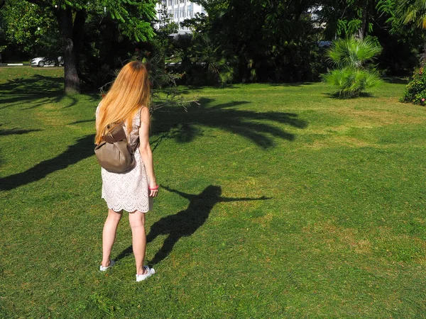 Uma menina fica em um gramado verde em uma posição relaxada e sua sombra segura as mãos nos lados — Fotografia de Stock