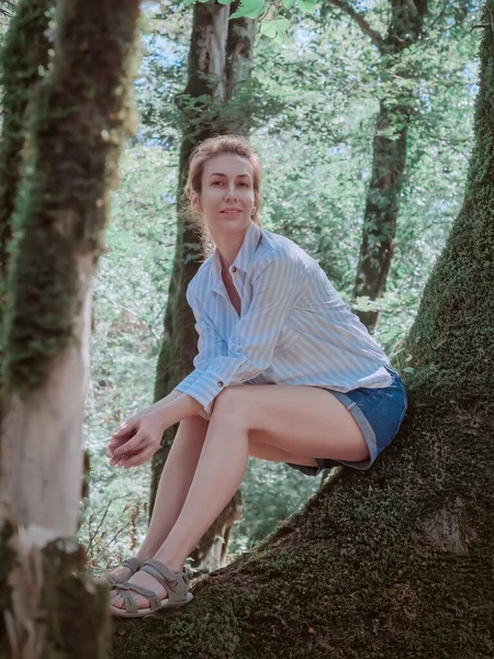 남부 숲에서 햇살을 받으며 성가신 나무줄기 위에 앉아 있는 미소짓는 소녀 — 스톡 사진