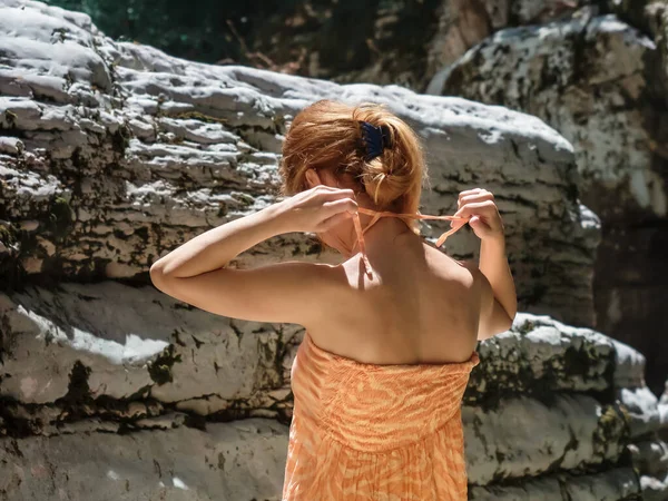 Una chica ata las correas de un vestido mientras está de pie sobre el fondo de los cañones de alivio bajo los rayos del sol brillantes —  Fotos de Stock