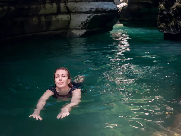 Chica sonriente nada en agua turquesa en una garganta sombría de cañones bajo los rayos del sol —  Fotos de Stock