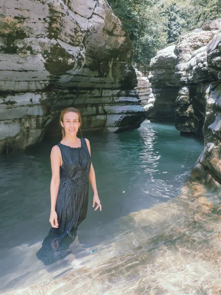 Χαμογελαστή κοπέλα με βρεγμένο φόρεμα στέκεται δίπλα στο νερό σε ένα σκιερό φαράγγι με φαράγγια. — Φωτογραφία Αρχείου