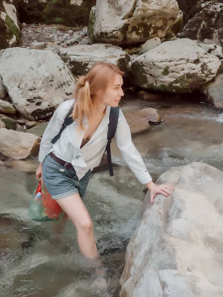 Ένας ταξιδιώτης διασχίζει ένα βραχώδες ποτάμι που βράζει κρατώντας μια πλακόστρωτη πέτρα με το χέρι της — Φωτογραφία Αρχείου
