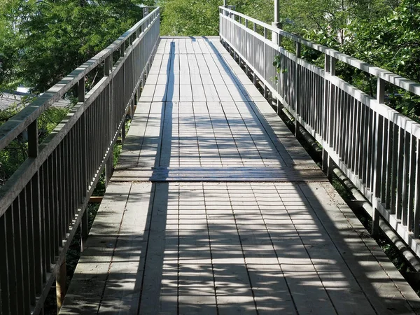 Dřevěný městský most se železným zábradlím osvětleným sluncem za letního dne. Perspektiva pohledu — Stock fotografie