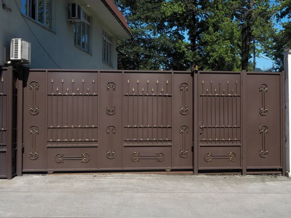 Portes automatiques brun fer et un guichet avec un motif forgé doré sur eux sont éclairés par le soleil — Photo