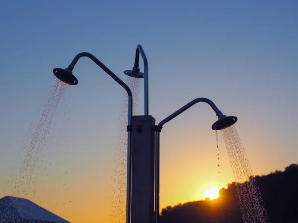 Jets of water pouring from a triple beach shower against the setting sun