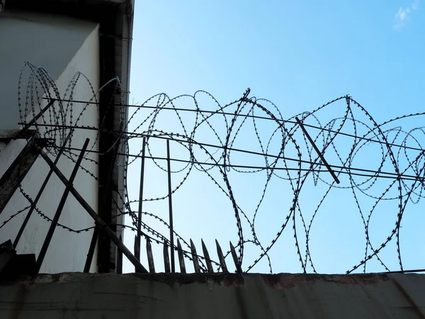 Fragment of an old concrete fence with barbed wire at the top against the blue sky — Stock Photo, Image