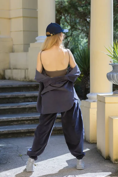 A girl in wide lilac clothes stands with her back bare in an old park architecture — Stock Photo, Image