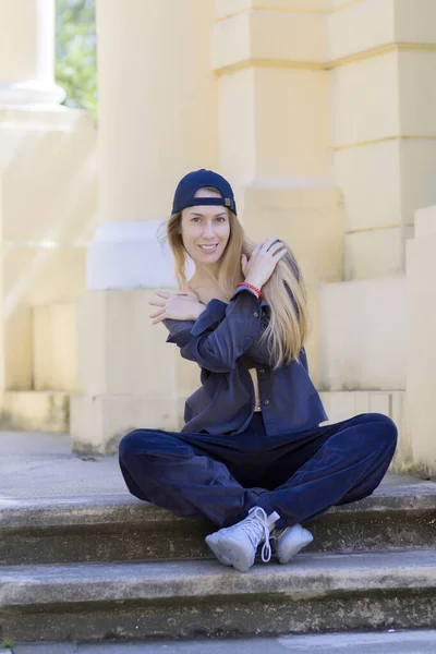 Sonriente rubia de pelo largo en ropa deportiva se sienta en los escalones de la arquitectura del parque — Foto de Stock