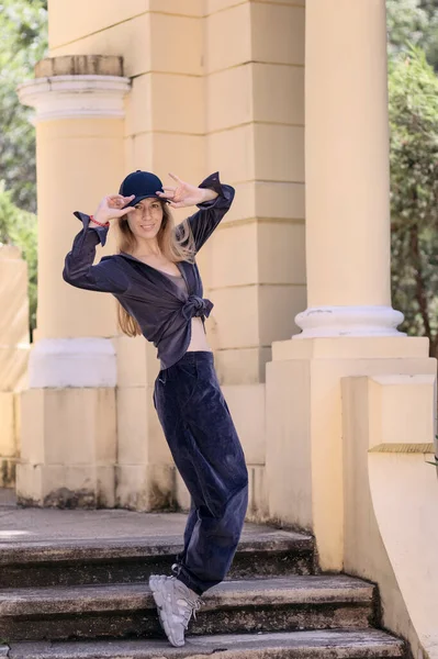 Chica alegre en estilo hip-hop se encuentra en los dedos de los pies en los escalones de la arquitectura del parque. Bailarina callejera — Foto de Stock