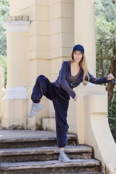 Una chica en un estilo deportivo se para con la rodilla levantada en los escalones del parque — Foto de Stock