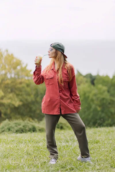 Sokak kıyafetli bir kız, yaz günü doğada bir tüpte milkshake içer.