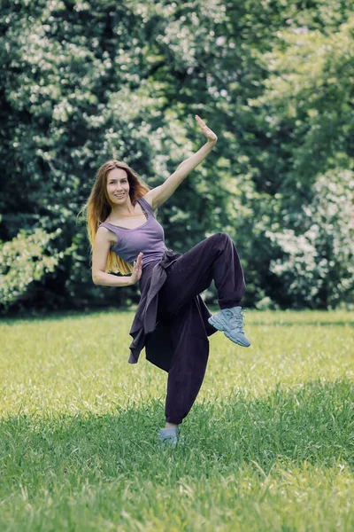 Smiling girl in lilac hip-hop outfit in a dance pose on the lawn in the park — Stock Photo, Image
