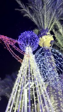 Bir Noel meleği yapısı, gece yarısı sicim ışıkları ve palmiye ağaçlarıyla aydınlatılıyor..