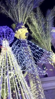 Palmiye ağaçları ve gece renkli çelenklerle süslenmiş bir Noel meleği..