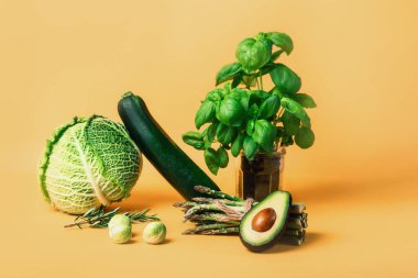 Lahana, kabak, kuşkonmaz, Brüksel lahanası, avokado ve turuncu arka planda fesleğen içeren soyut kompozisyon. Vejetaryen ve vejetaryen diyeti. Sürdürülebilir yaşam tarzı, bitkisel gıdalar.
