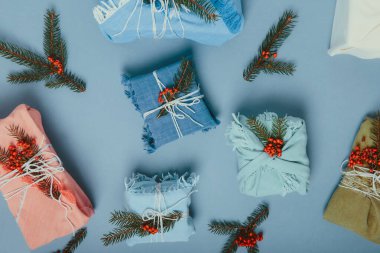 Sıfır noel ziyanı konsepti. Ladin dallı kumaşa sarılı hediye kutuları ve sessiz mavi arka planda böğürtlenler. Flatlay. Çevre dostu, sürdürülebilir yaşam. Plastik yok. Boşluğu kopyala.