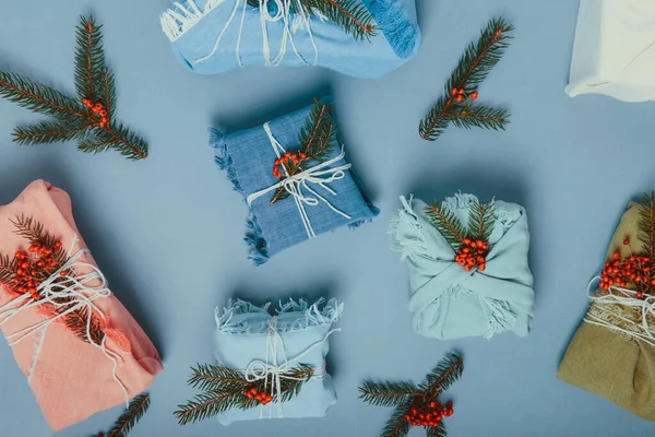 Top view zero waste christmas concept. Gift boxes wrapped in fabric with spruce branch and berries on muted blue background. Flatlay. Eco friendly Sustainable lifestile. No plastic. Copy space.