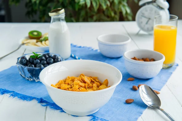 Nährstoffreiches gesundes Frühstück. Schüssel mit Müsli, Mandeln, Blaubeeren, pflanzlicher Milch und Orangensaft auf blauer Serviette und weißem Holztisch. Ernährungsplanung und gesundes Ernährungskonzept. — Stockfoto