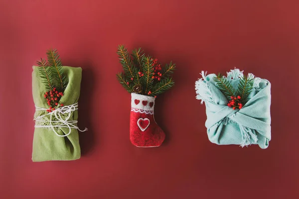 Festive Christmas composition of decorative felt sock with spruce branches and gift boxes wrapped in fabric and natural decor on rich burgundy color background. Vintage toning Christmas background. — Stock Photo, Image