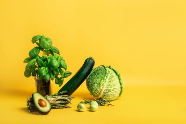 Lahana, kabak, kuşkonmaz, Brüksel lahanası, avokado ve sarı arka planda fesleğen içeren soyut kompozisyon. Vejetaryen ve vejetaryen diyeti. Sürdürülebilir yaşam tarzı, bitkisel gıdalar.