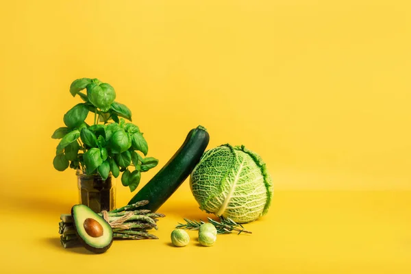 Composición abstracta con verduras frescas de col, calabacín, espárragos, coles de Bruselas, aguacate, albahaca sobre un fondo amarillo. Dieta vegetariana y vegana. Estilo de vida sostenible, alimentos a base de plantas. —  Fotos de Stock