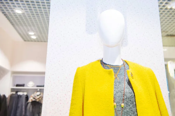 Female mannequin in the bright yellow coat and grey top on the showcase of a fashion store. Trendy colors of 2021 in the shopping Mall. Selective focus. Space for text.
