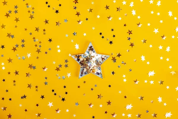 Big star shape with sparling golden and silver stars among star shape glittering confetti on the yellow background. Festive concept. Be unique, to shine bright. Selective focus. Flatlay, top view.