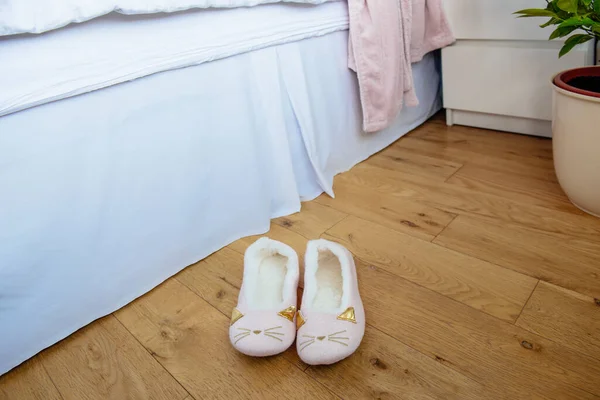 Female or child pink comfort slippers on the wooden floor near the bed. Funny home kitty slippers. Morning habits. Selective focus, copy space. — Stock Photo, Image