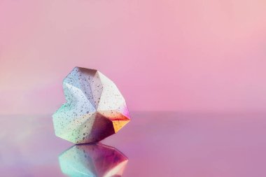 Parlak geometrik kalp, parlak pembe bir arka planda yansıması var. Noktalı beyaz ve pembe çokgen kalp yüzeyde yatıyor. Modern Yaratıcı Sevgililer Günü kartı. Minimalist stil.