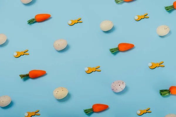 Renkli yumurtalardan, dekoratif havuçlardan ve pastel mavi arka planda sarı tavşanlardan oluşan paskalya deseni. Minimum festival bahar konsepti — Stok fotoğraf