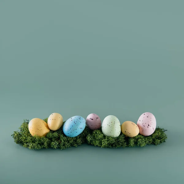Arka plandaki yosunların üzerine yerleştirilmiş Paskalya renkli yumurtalar. Mutlu Paskalyalar. Sönük renkler. Kare kart. Seçici odaklanma. Boşluğu kopyala. — Stok fotoğraf
