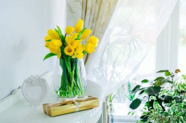 Bir buket taze sarı bahar lalesi ve nergis çiçekleri, altın hediye kutusu ve göğüs çekmecesindeki kalp şeklinde çerçeve hafif klasik iç tasarım. Kadınlar günü kutlaması, tebrik kartı.